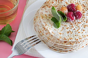 Fried pancakes close-up on a white plate, pancakes with raspberries, tea cerimonia, dessert on a pink background