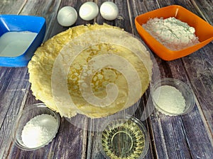 Fried pancakes, wheat flour, milk, chicken eggs, vegetable oil, salt and sugar on a wooden table.  Ingredients for fried pancakes