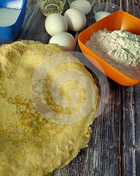 Fried pancakes, wheat flour, milk, chicken eggs, vegetable oil, salt and sugar on a wooden table.  Ingredients for fried pancakes