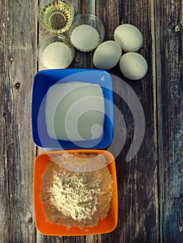 Fried pancakes, wheat flour, milk, chicken eggs, vegetable oil, salt and sugar on a wooden table.  Ingredients for fried pancakes