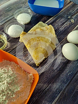 Fried pancakes, wheat flour, milk, chicken eggs, vegetable oil, salt and sugar on a wooden table.  Ingredients for fried pancakes