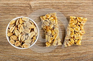 Fried peanuts in bowl, pieces of kozinak on wooden table. Top view