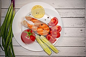 Fried piece of salmon on a white plate with tomatoes, onions, cucumbers, on the boards