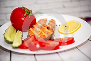 Fried piece of salmon on a white plate with tomatoes, onions, cucumbers, on the boards