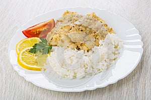 Fried pollock with rice, lemon, parsley, tomato in plate