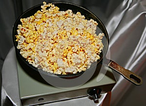 Fried popcorn in an old cast iron skillet on the light green vintage electric tile on the background of gray-silver fabric draping