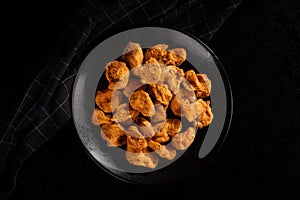 Fried pork cracklings on black plate on dark background