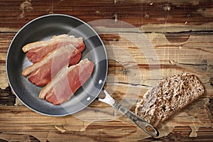 Prosciutto Rashers In Teflon Frying Pan And Slice Of Brown Bread Set On Old Cracked Flaky Wooden Garden Table photo