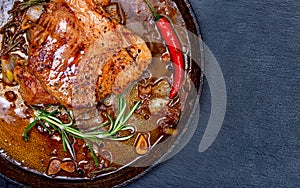 Fried pork meat in frying pan over dark background, top view. Chili pepper and rosemary