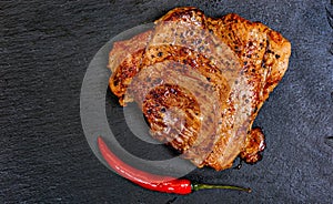 Fried pork meat in frying pan over dark background, top view. Chili pepper and rosemary