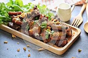 Fried pork ribs with garlic and cilantro dressing on top in wooden plate