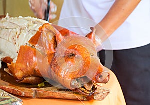 Fried pork on table. Waiter cut whole pork. Traditional dish whole roasted pig with head.