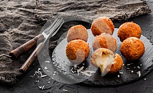 Fried potato cheese balls or croquettes with spices on black plate over dark stone background