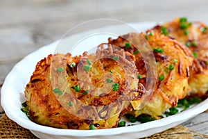 Fried potato pancakes or draniki with ham slices and green onion on a white plate. Simple draniki recipe. Closeup