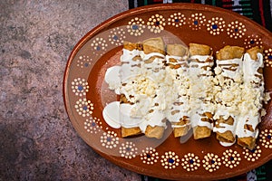Fried potato tacos with cream and cheese in a Mexican mud dish. Tacos dorados photo