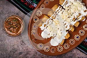 Fried potato tacos with cream and cheese in a Mexican mud dish. Tacos dorados photo