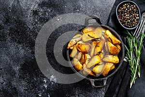 Fried potato wedges, French fries in a pan. Black background. Top view. Copy space