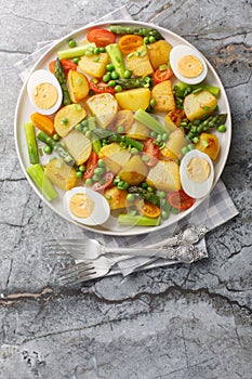 Fried potatoes with asparagus, cherry tomatoes, egg and green peas close-up in a plate. Vertical top view