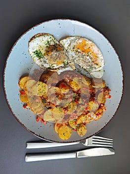 Fried potatoes with bacon cubes and fried eggs