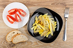 Fried potatoes in black plate, tomatoes, bread and fork