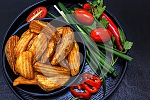 Fried potatoes on a black wooden plate with fresh vegetables - onions, tomatoes, parsley