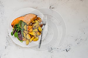 Fried potatoes with fish and green salad on a white plate