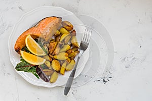 Fried potatoes with fish and green salad on a white plate