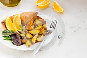 Fried potatoes with fish and green salad on a white plate