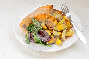 Fried potatoes with fish and green salad on a white plate