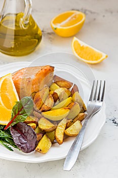 Fried potatoes with fish and green salad on a white plate