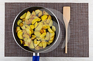 Fried potatoes in frying pan, spatula on mat on table. Top view