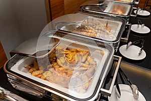 Fried potatoes garnish and meat on skewers in a food warmer on a buffet table in a hotel restaurant