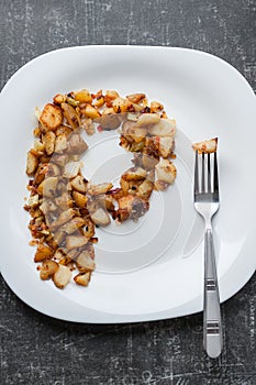 Fried potatoes lie in a plate on a black table with a fork