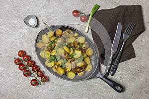 Fried potatoes with mushrooms and onion in iron pan at gray background