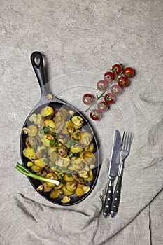 Fried potatoes with mushrooms and onion in iron pan at gray background