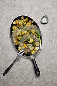 Fried potatoes with mushrooms and onion in iron pan at gray background