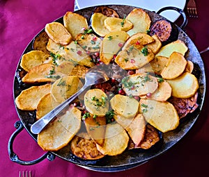 Fried potatoes in wedges with eggplant and pomegranate seeds in large frying pan