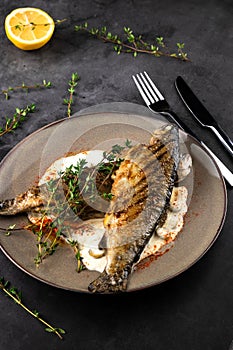 Fried rainbow trout fish with lemon sauce and thyme on black marble table as background