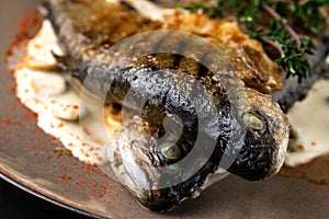 Fried rainbow trout fish with lemon sauce and thyme on black marble table as background. macro view