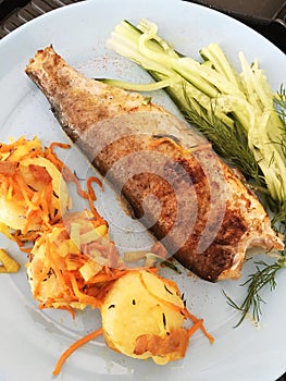 fried rainbow trout with potatoes, vegetables and spices on a plate