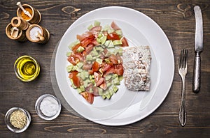 Fried red fish with sauce and garnished with vegetable salad on white plate with spices vintage knife and fork on wooden rusti