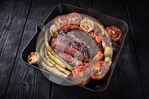 Fried rib eye steak in a cut in a cast iron pan with vegetables.