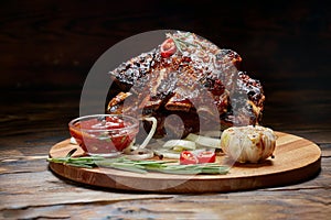 Fried ribs with rosemary, onion, sauce on a wooden round Board. Dark background. ace