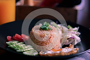 Fried rice, fried egg, cucumber, sliced tomato, green salad and Fried chicken placed on a black plate as a garnish