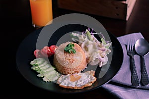 Fried rice, fried egg, cucumber, sliced tomato, green salad and Fried chicken placed on a black plate as a garnish
