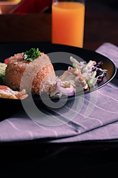 Fried rice, fried egg, cucumber, sliced tomato, green salad and Fried chicken placed on a black plate as a garnish