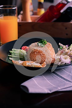 Fried rice, fried egg, cucumber, sliced tomato, green salad and Fried chicken placed on a black plate as a garnish