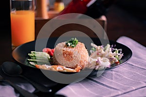 Fried rice, fried egg, cucumber, sliced tomato, green salad and Fried chicken placed on a black plate as a garnish