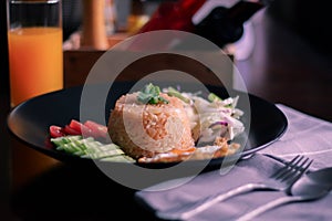 Fried rice, fried egg, cucumber, sliced tomato, green salad and Fried chicken placed on a black plate as a garnish