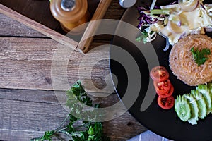 Fried rice, fried egg, cucumber, sliced tomato, green salad and Fried chicken placed on a black plate as a garnish